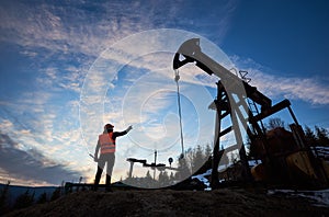 Petroleum operator pointing at oil well pump jack.