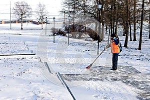 A woman with a broom sweeps snow from a stone staircase in the early morning. A public service worker.