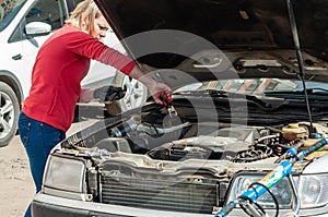 A young woman at the open bonnet of a car is trying to fix the malfunction