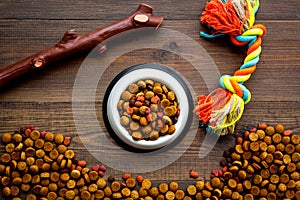 Pets accessories in home. Dog food in bowl and toys on dark wooden background top view