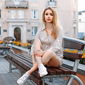 Petty woman in white sneakers sits on a bench on the background