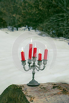 Pewter candelabra with five red burning candles stands on tree trunk outside in winter