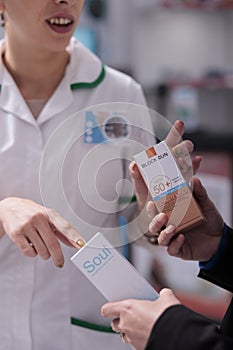 Pharmaceutical assistant advising customer sunblock and pointing on package