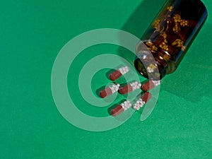 Pharmaceutical capsules and glass bottle on green background.