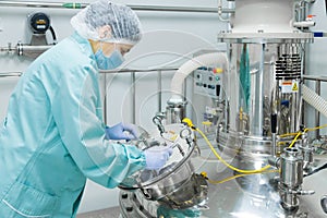 Pharmaceutical factory woman worker in protective clothing operating production line in sterile environment