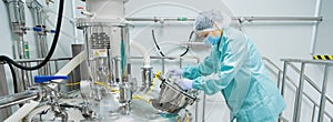 Pharmaceutical factory woman worker in protective clothing operating production line in sterile environment