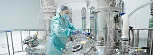 Pharmaceutical factory woman worker in protective clothing operating production line in sterile environment