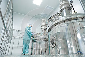 Pharmaceutical factory woman worker in protective clothing operating production line in sterile environment