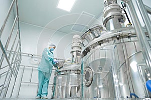 Pharmaceutical factory woman worker in protective clothing operating production line in sterile environment