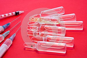 Pharmaceutical glass vials or ampules with liquid drug inside lie near syringes with needles on red uniform background. Concept pr