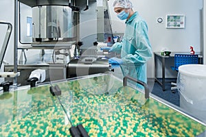 Pharmaceutical industry man worker in protective clothing operating production of tablets in sterile working conditions