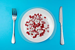 Pharmaceutical medicine pills or capsules on a plate with a fork and knife