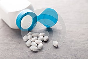 Pharmaceutical medicine tablets, pills, capsules, drugs on grey background in white and blue plastic jar. Pill bottle
