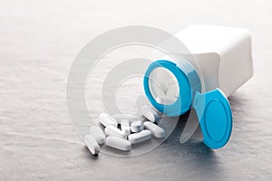 Pharmaceutical medicine tablets, pills, capsules, drugs on grey background in white and blue plastic jar. Pill bottle