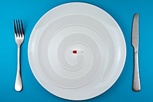 Pharmaceutical pill or capsule on a plate with a fork and knife
