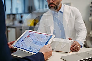 Pharmaceutical sales representative presenting new medication to doctor in medical building, holding tablet with