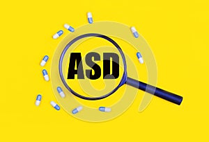 Pharmaceutical tablets and capsules near a magnifying glass with the text ASD Autism Spectrum Disorder on a yellow background.