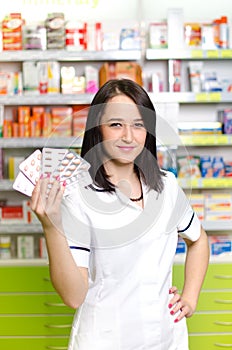 Pharmacist chemist woman show a pill. Pharmacy drugstore is background. Pretty, young laborant.