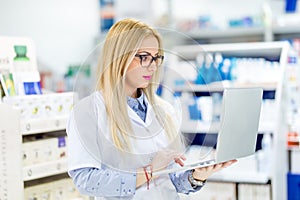 Pharmacist chemist woman standing in pharmacy drugstore and using laptop for network social media