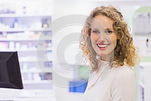 Female pharmacy staff smiling while checking computer monitor and organizing shelves, copy space
