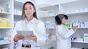 Pharmacist with digital tablet while doing stock update and counting inventory with a colleague in a pharmacy. Female