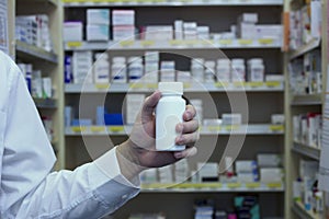 Pharmacist holding white vitamin bottle in front of dispensary shelves photo