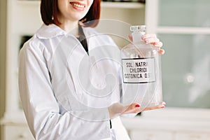 Pharmacist in lab holding glass bottle with natrium chloride