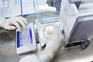 Laboratory worker in sterile rubber gloves, weighs the manufactured tablets on the control scales.