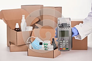 Pharmacist's hand holding a POS terminal in front of boxes with medications