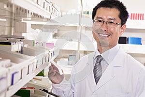 Pharmacist taking down and examining prescription medication in a pharmacy, looking at camera