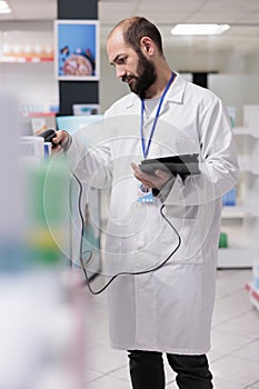 Pharmacist in white coat holding tablet computer typing vitamins barcode while doing drugs inventory