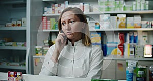 A pharmacist woman stands in a pharmacy against the background of drugs and talks on the phone. Working conversations