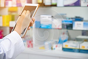 Pharmacist working with a tablet computer in the pharmacy holding it in her hand while reading information