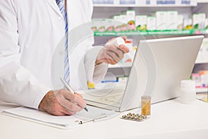 Pharmacist writing on clipboard and holding medication