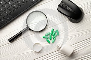 Pharmacological capsules and magnifier with keyboard and computer mouse on a white wooden table