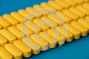 Pharmacology industry produce concept of many rows of yellow pills tablets of vitamin drugs on blue surface