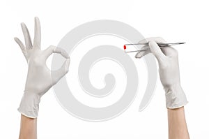 Pharmacology and Medical theme: doctor's hand in a white glove holding tweezers with red pill capsule isolated on white background