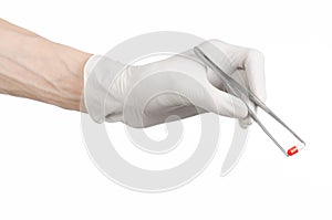 Pharmacology and Medical theme: doctor's hand in a white glove holding tweezers with red pill capsule isolated on white background