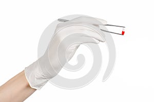 Pharmacology and Medical theme: doctor's hand in a white glove holding tweezers with red pill capsule isolated on white background photo