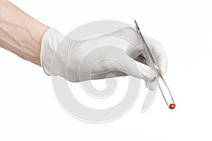 Pharmacology and Medical theme: doctor's hand in a white glove holding tweezers with red pill capsule isolated on white background