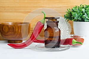 Pharmacy bottle with red chili pepper extract tincture, infusion, oil and fresh chili pepper pods.