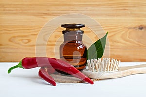 Pharmacy bottle with red chili pepper extract tincture, infusion, oil, fresh chili pepper pods and wooden hair brush.