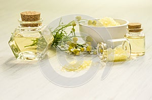 Pharmacy chamomile flower, water or infusion in glass bottles and bath or SPA salt on white wooden background