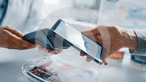 Pharmacy Drugstore Checkout Cashier Counter: Pharmacist and a Customer Using NFC Smartphone with