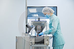 Pharmacy industry woman worker in protective clothing operating production of tablets in sterile working conditions