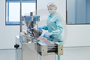 Pharmacy industry woman worker in protective clothing operating production of tablets in sterile working conditions