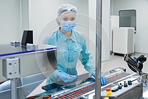 Pharmacy industry woman worker in protective clothing operating production of tablets in sterile working conditions