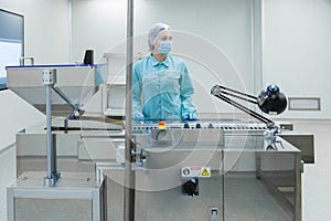 Pharmacy industry woman worker in protective clothing operating production of tablets in sterile working conditions