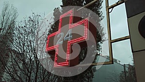 Pharmacy sign, red cross pharmacy sign or symbol on the building facade view from the street against a cloudy sky