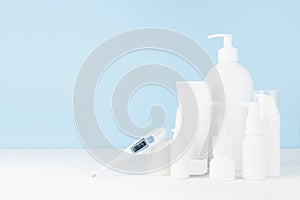 Pharmacy white plastic bottles, sprays, salve, creams mockup with 36,6 thermometer on white table and soft light blue wall.